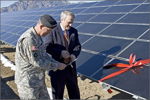 Photo of two men standing in front of a solar array ready to cut a red ribbon with scissors.