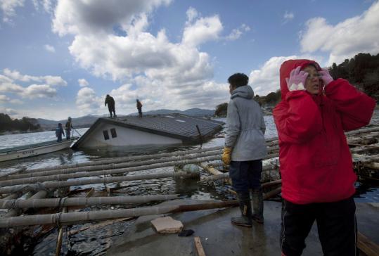 Reiko Kikuta (right) and her husband, Takeshi, waited on the shore of Oshima Island in northeastern Japan yesterday as workers attempted to attach ropes to their submerged home to try to pull it ashore using construction equipment.