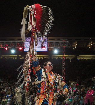 Not long before the afternoon grand entry, a dancer raises a warbonnet as spectators cheered and snapped photographs.