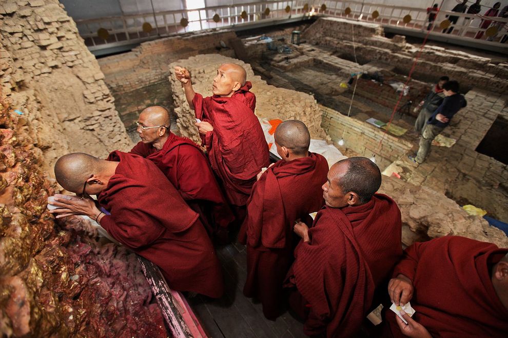 Pilgrims meditate at the wall below the nativity scene within the Maya Devi Temple at Lumbini, Nepal. The remains of the earliest temples at the site are in the background.