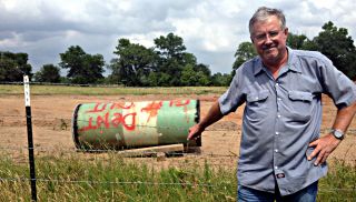 David Whitley stands near his fence in front of a piece of removed pipe labeled "Dent Cut Out." Credit: Public Citizen
