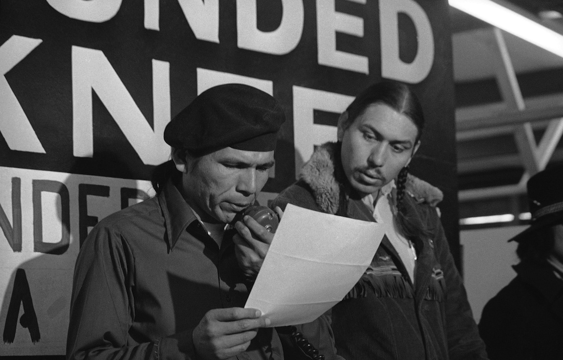 In this March 18, 1973 file photo taken in Wounded Knee, S.D., American Indian Movement leader Dennis Banks, left, reads an offer by U.S. government seeking to effect an end to the takeover of Wounded Knee. Looking on is AIM leader Carter Camp. Camp, a longtime activist with the American Indian Movement who was a leader in the Wounded Knee occupation in South Dakota, died Dec. 27, 2013, in White Eagle, Okla. He was 72. (AP Photo/Jim Mone, File)