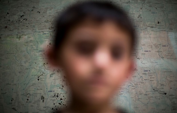 In this June 19, 2014 photo, a Guatemalan child deported from the United State poses for photo in front of a map of the Guatemala City at an immigration shelter in Guatemala City. The number of unaccompanied minors detained on the U.S. border has more than tripled since 2011. (AP/Luis Soto)