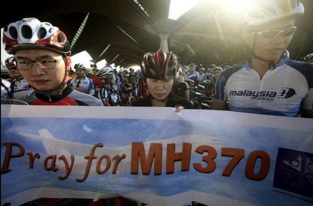 Cyclists hold a banner as they take a moment of silence and pray during "The Ride of Prayer" for the missing Malaysia Airlines, flight MH370, outside the departure hall of Kuala Lumpur International Airport in Sepang, Malaysia, Sunday, March 23, 2014. Search planes headed back out to a desolate patch of the southern Indian Ocean on Sunday in hopes of finding answers to the fate of the missing Malaysia Airlines jet, after China released a satellite image showing a large object floating in the search zone. (AP Photo/Joshua Paul)