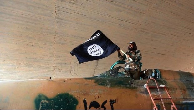 This undated image posted on Wednesday, Aug. 27, 2014 by the Raqqa Media Center of the Islamic State group, a Syrian opposition group, which has been verified and is consistent with other AP reporting, shows a fighter of the Islamic State group waving their flag from inside a captured government fighter jet following the battle for the Tabqa air base, in Raqqa, Syria on Sunday. (AP Photo/ Raqqa Media Center of the Islamic State group) 