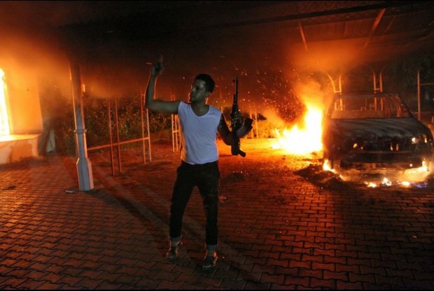 An armed man waves his rifle as buildings and cars are engulfed in flames after being set on fire inside the US consulate compound in Benghazi late on September 11, 2012. (Photo Credit: AFP/Getty Images)