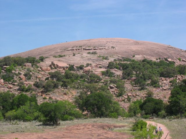 Enchanted Rock is considered sacred by the Comanche. It is seen here from the trail leading to the summit. People climbing on the summit (visible as dots) give an idea of the scale of the granite rock. (Wikipedia)