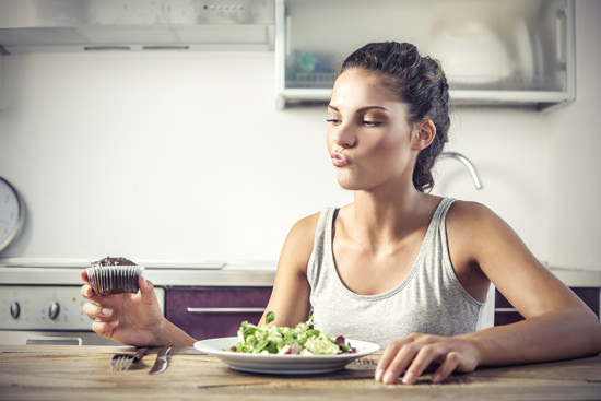 Young Woman Deciding Whether to Eat a Salad or a Muffin