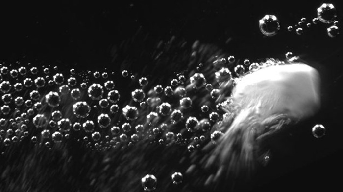 Image showing a carbonate particle releasing carbon dioxide and propelling at a high velocity through an ...