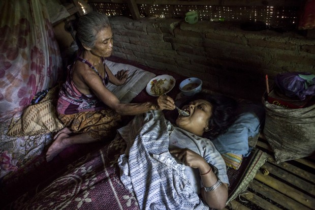Sijum, 40, who suffers from Down syndrome, eats while assisted by her mother Toyimah inside a house at Sidoarjo Village in Jambon subdistrict on March 25, 2016 in Ponorogo district, Indonesia. Sijum, has been paralyzed and mute since she was a baby. (Photo by Ulet Ifansasti/Getty Images)