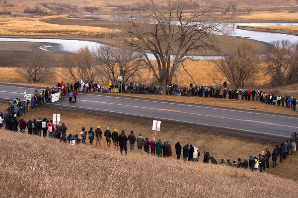 Water protectors stand in a peaceful ceremonial circle on Highway 1806 just south of where Backwater Bridge crosses Cantapeta Creek. Armed police have blockaded the bridge with concrete barriers, razor wire, and vehicles. (Photo: Amy Gulick)