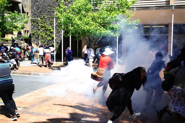 Students run away from a stun grenade that South African police used to disperse the students after they broke windows at the University of Cape town campus in Cape Town, South Africa, Monday, Oct. 17, 2016. (AP Photo/Schalk van Zuydam)