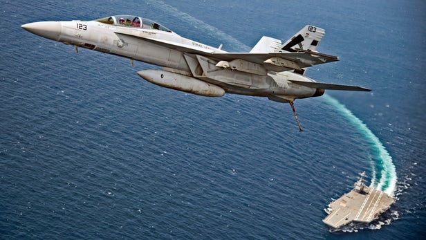 An F/A-18F Super Hornet assigned to Air Test and Evaluation Squadron (VX) 23 flies over USS ...