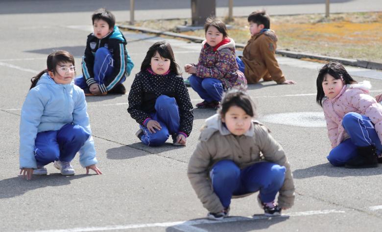 Elementary school students squat down on the street as they participate in an evacuation drill for local residents based on the scenario that a ballistic missile launched landed in Japanese waters, in Oga, Akita prefecture, Japan March 17, 2017.  Kyodo/via REUTERS